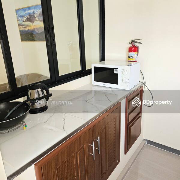 Kitchen pantry with microwave, kettle, pots, pan, spatula, and chopping board.